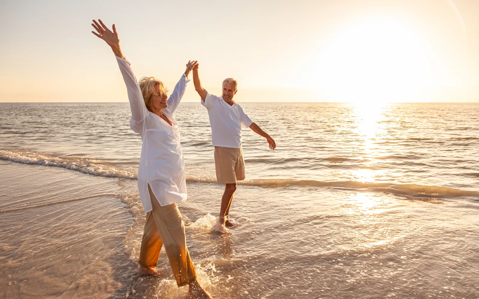 Retired couple dancing and playing in the surf on a beach at sunset.