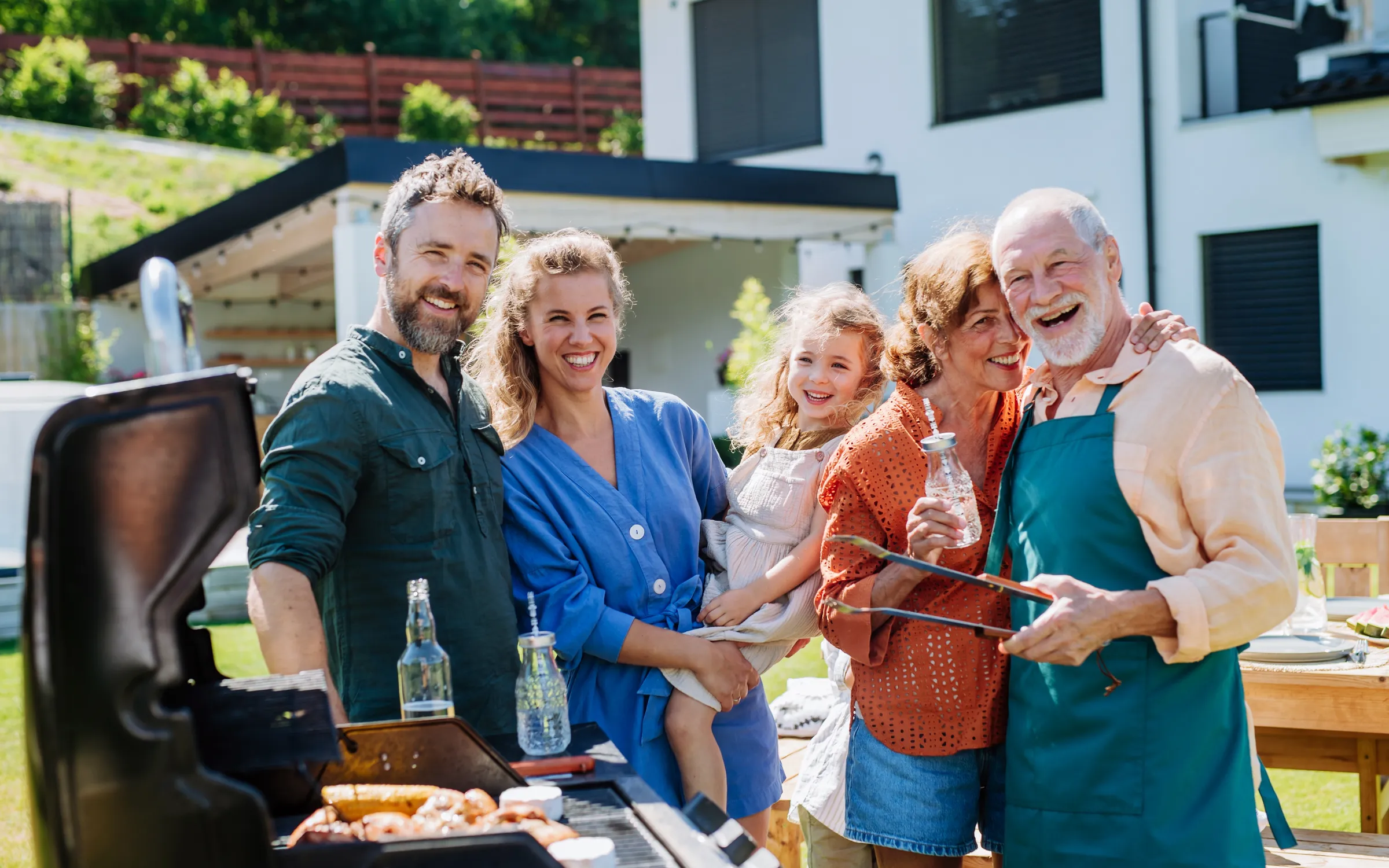 Multigenerational family laughing together at a backyard barbecue on a sunny afternoon.