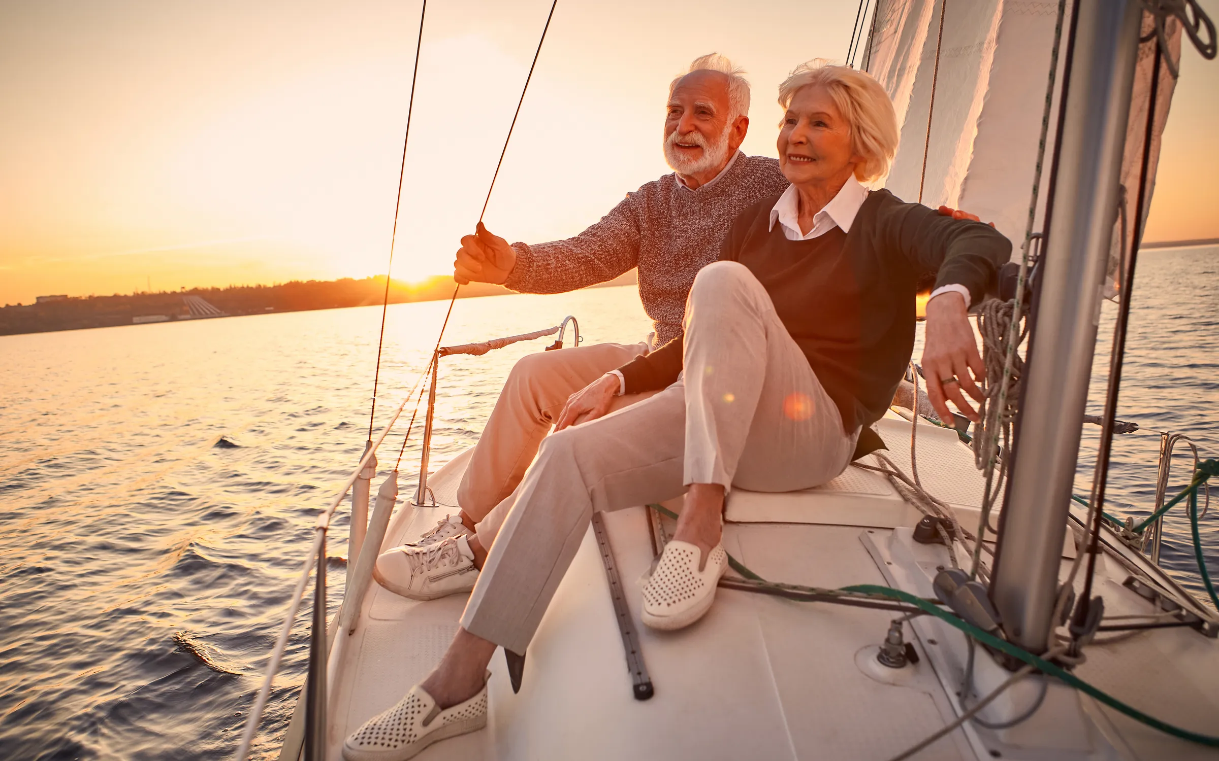 Retired couple sailing together on open water at sunset.